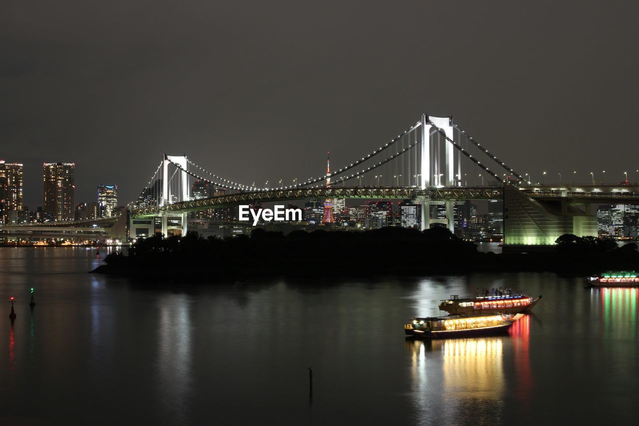 Illuminated rainbow bridge over river against sky at night