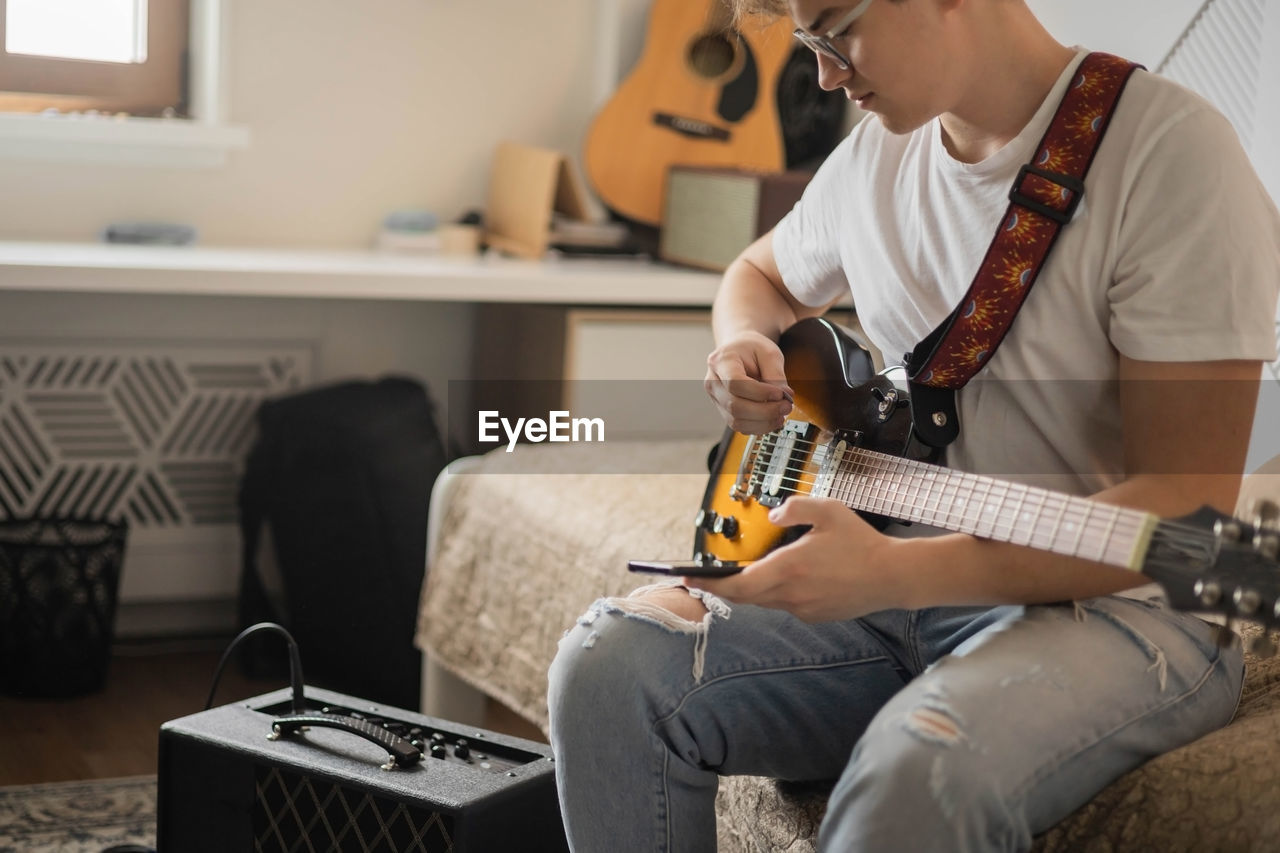 midsection of man playing guitar at home