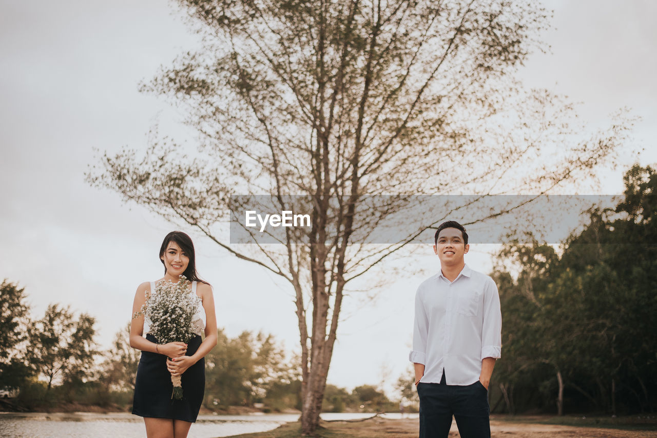 Portrait of smiling young couple standing against tree