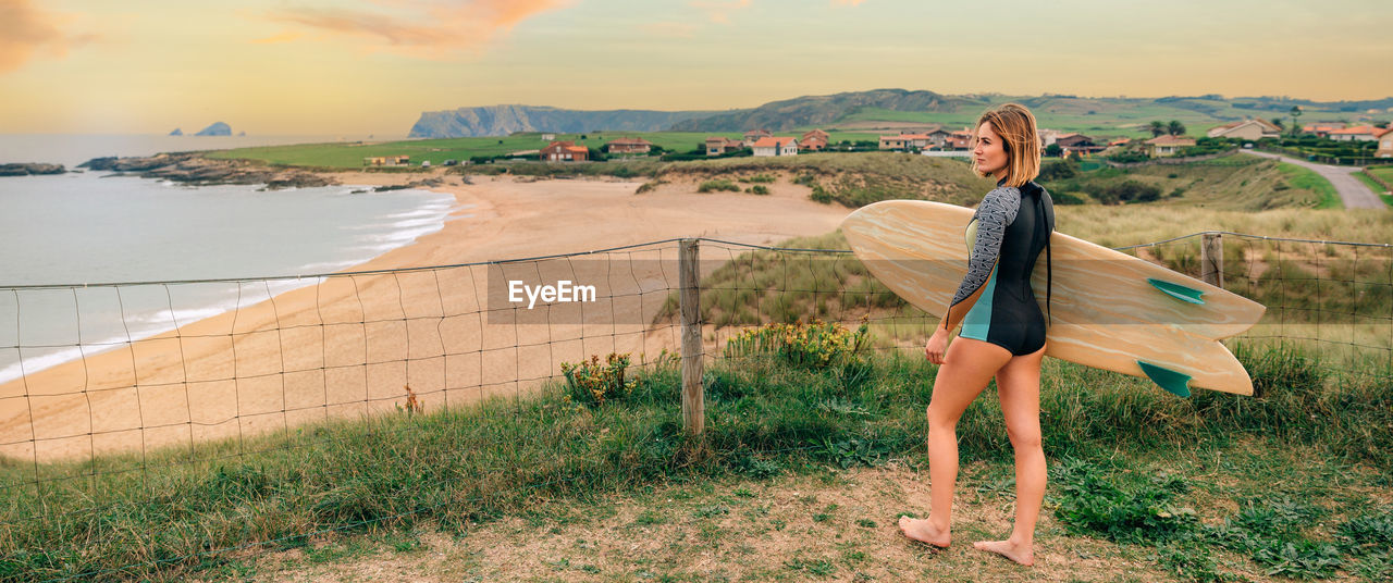 Surfer woman with wetsuit and surfboard looking at the beach