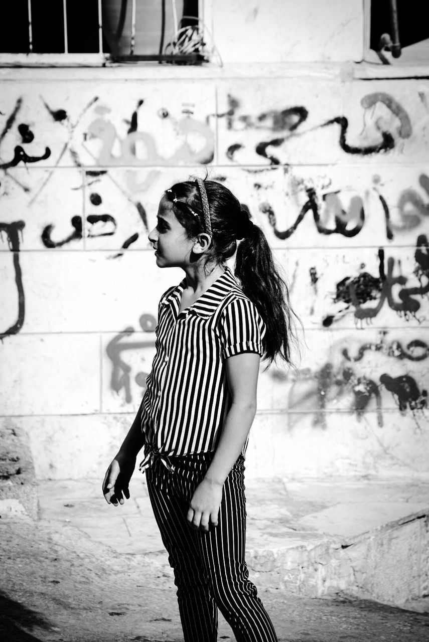 FULL LENGTH OF HAPPY YOUNG WOMAN STANDING AGAINST GRAFFITI