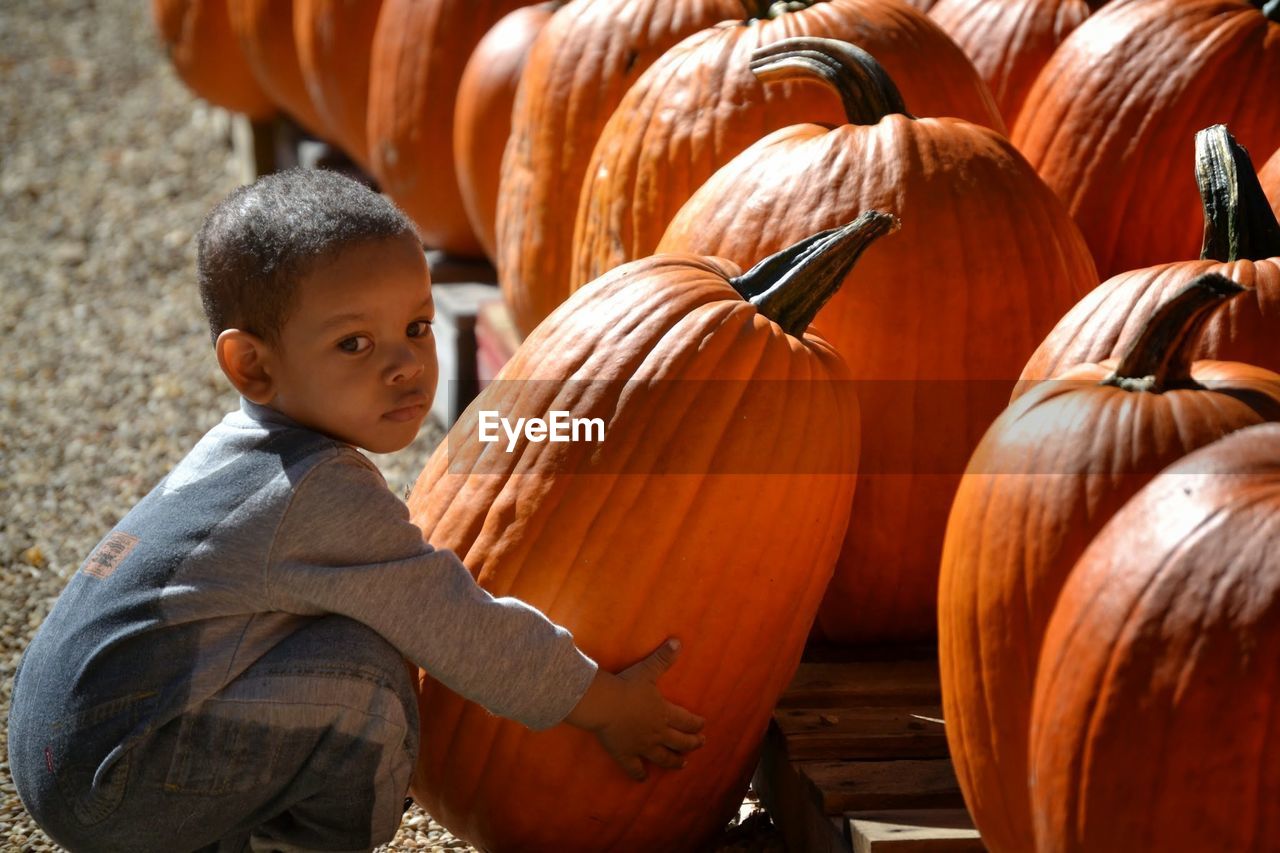 Side view of boy holding pumpkin on field