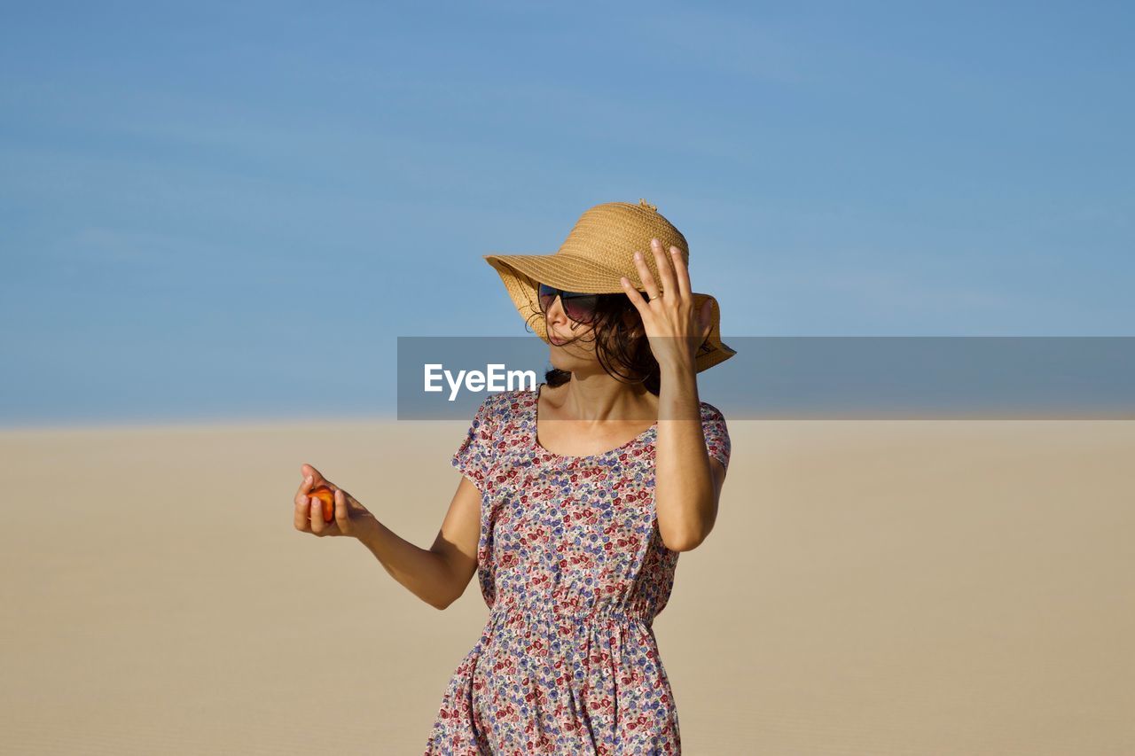 Woman in hat standing at beach against sky