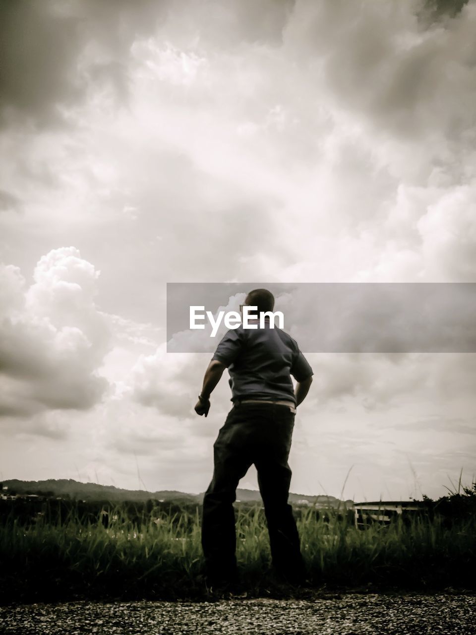 Rear view of man standing on field against clouds