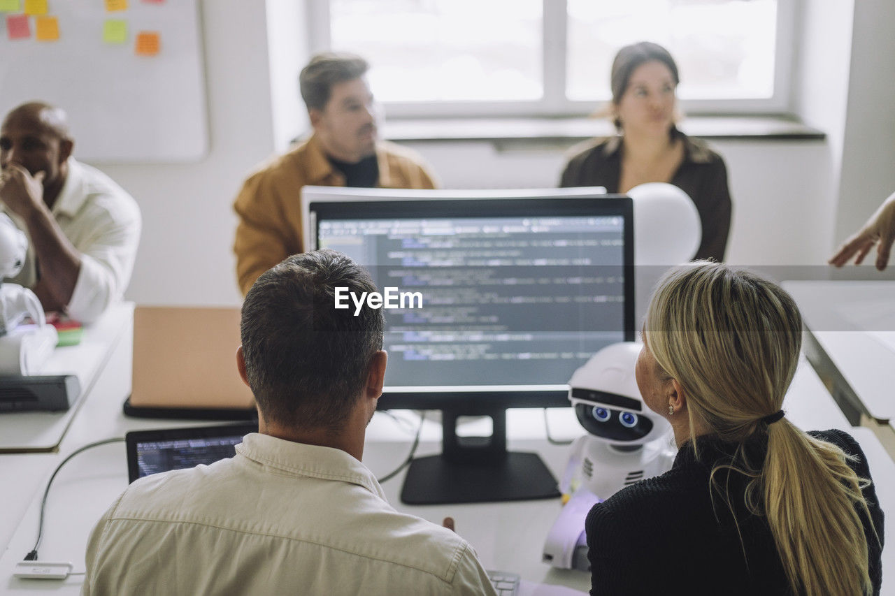 Rear view of professor discussing with student over computer at desk in innovation lab