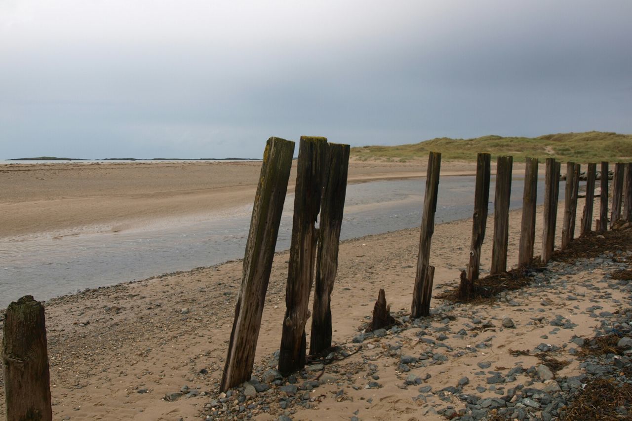 Wooden posts on beach against sky