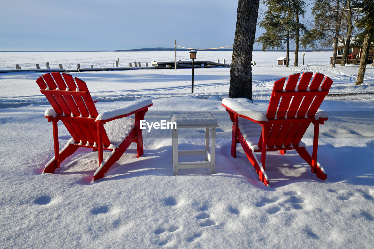 Red adirondack chair along the frozen shore in winter snow