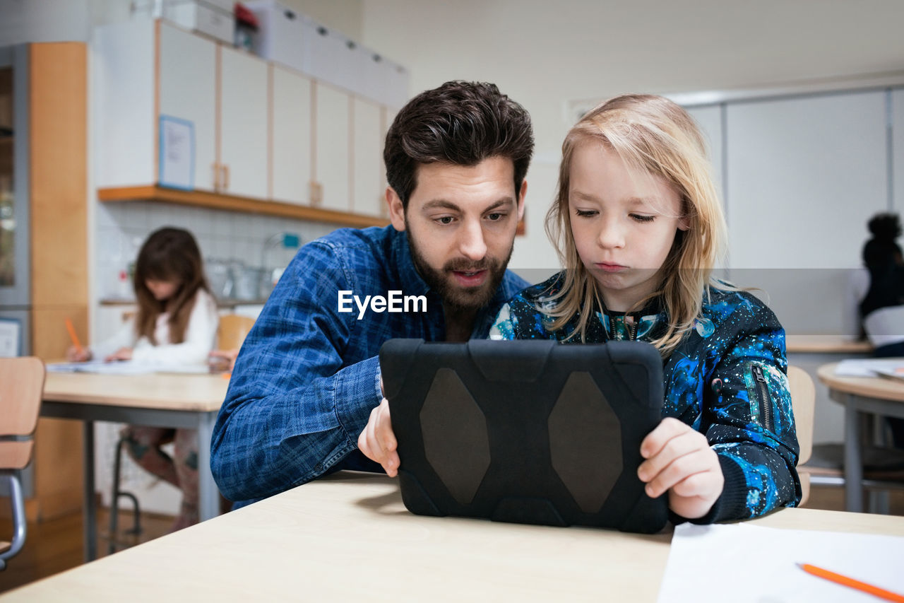 Male teacher explaining student in using digital tablet at classroom