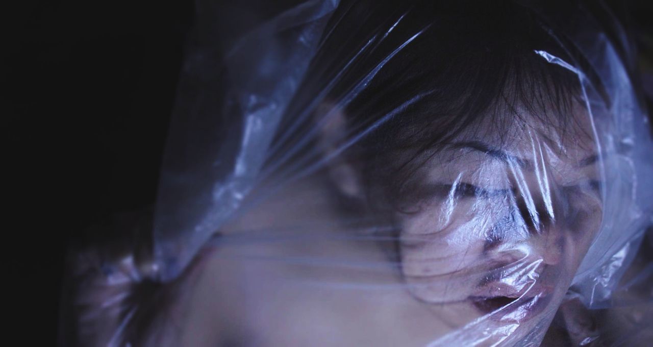 Close-up of woman wrapped in plastic against black background