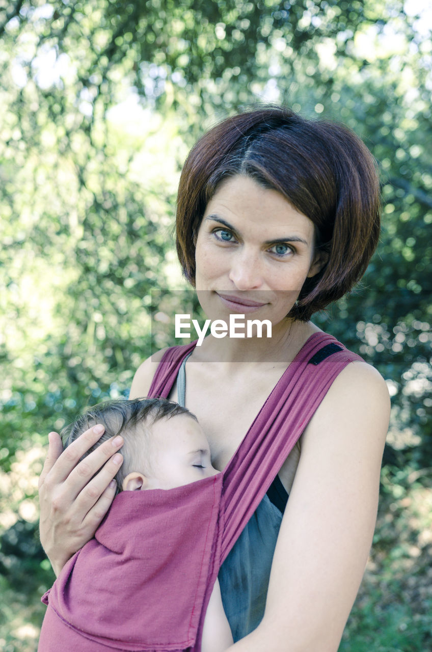 Portrait of mother carrying toddler daughter against trees