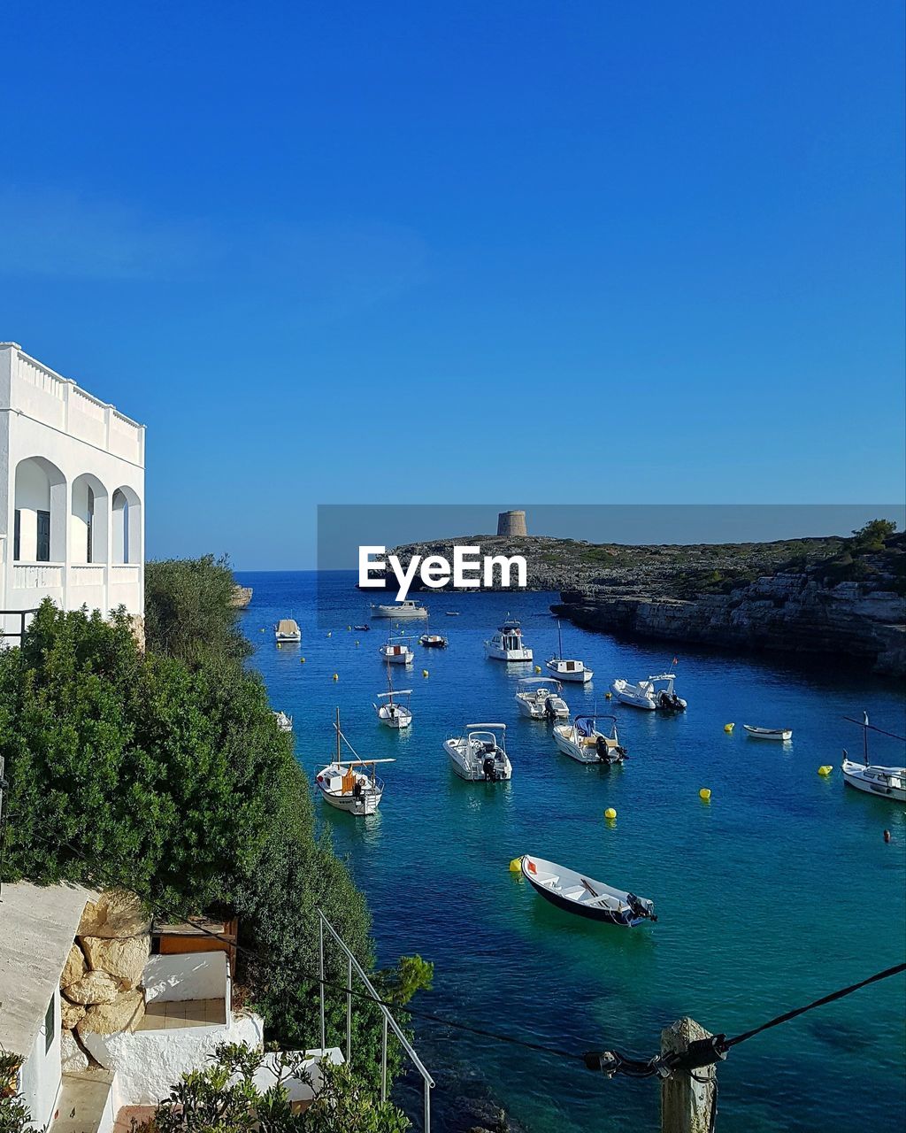 Sailboats in sea by buildings against clear blue sky