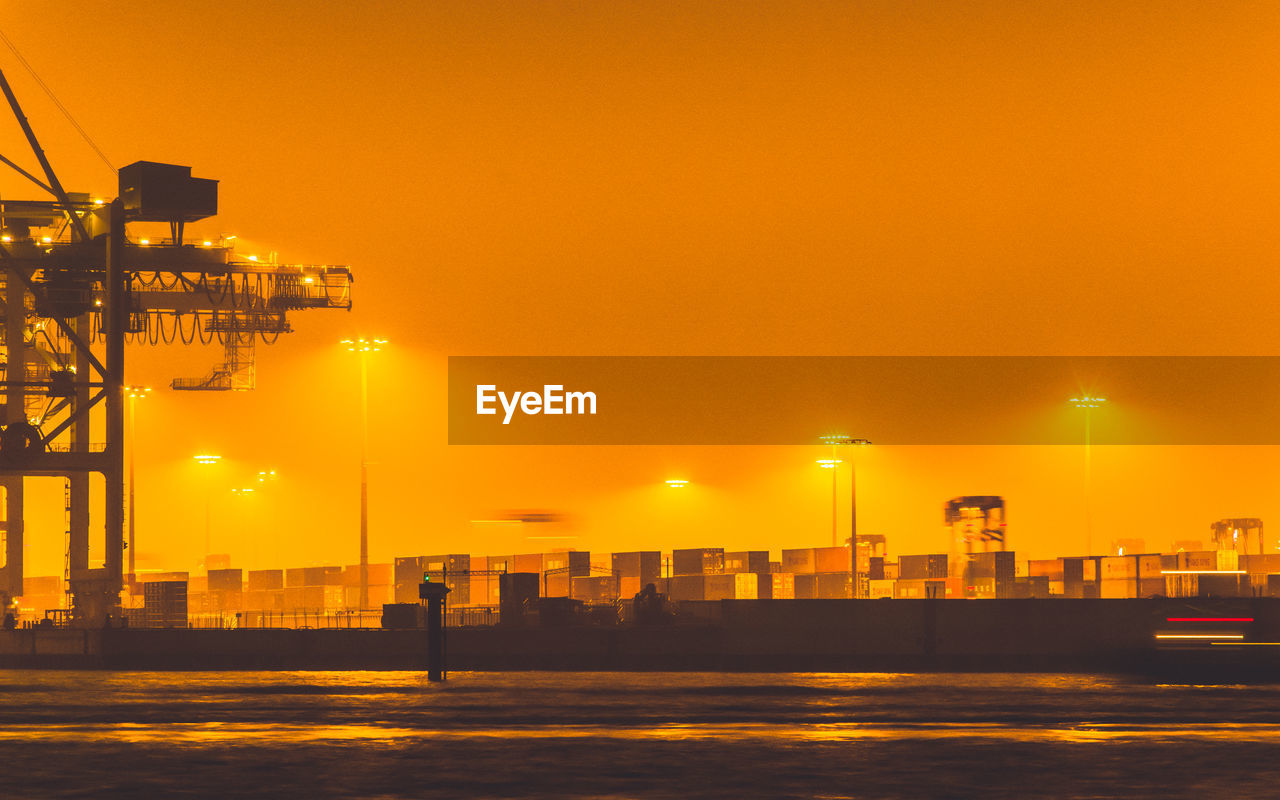 Illuminated buildings by sea against sky during sunset