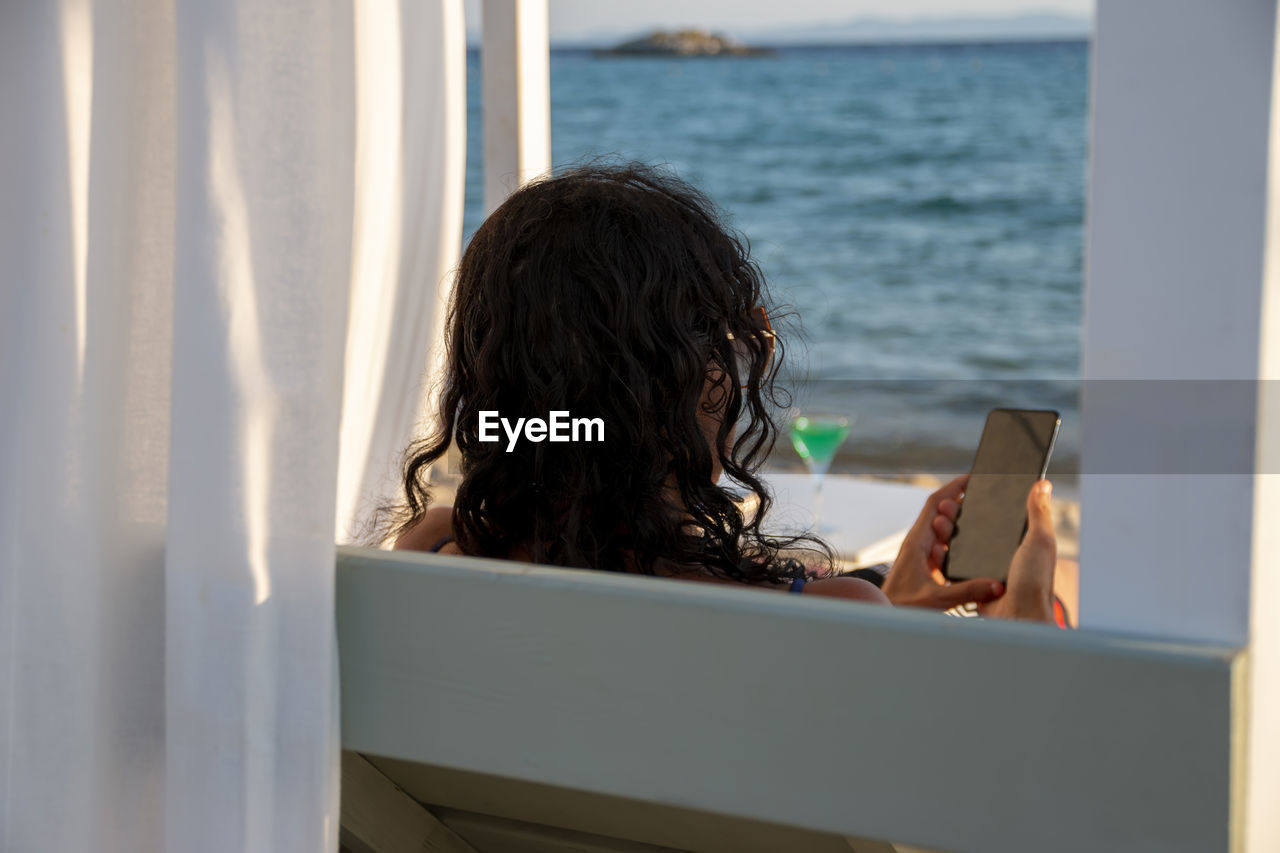 Middle-aged woman on vacation relax in daybed holding her smart phone chatting with and technology