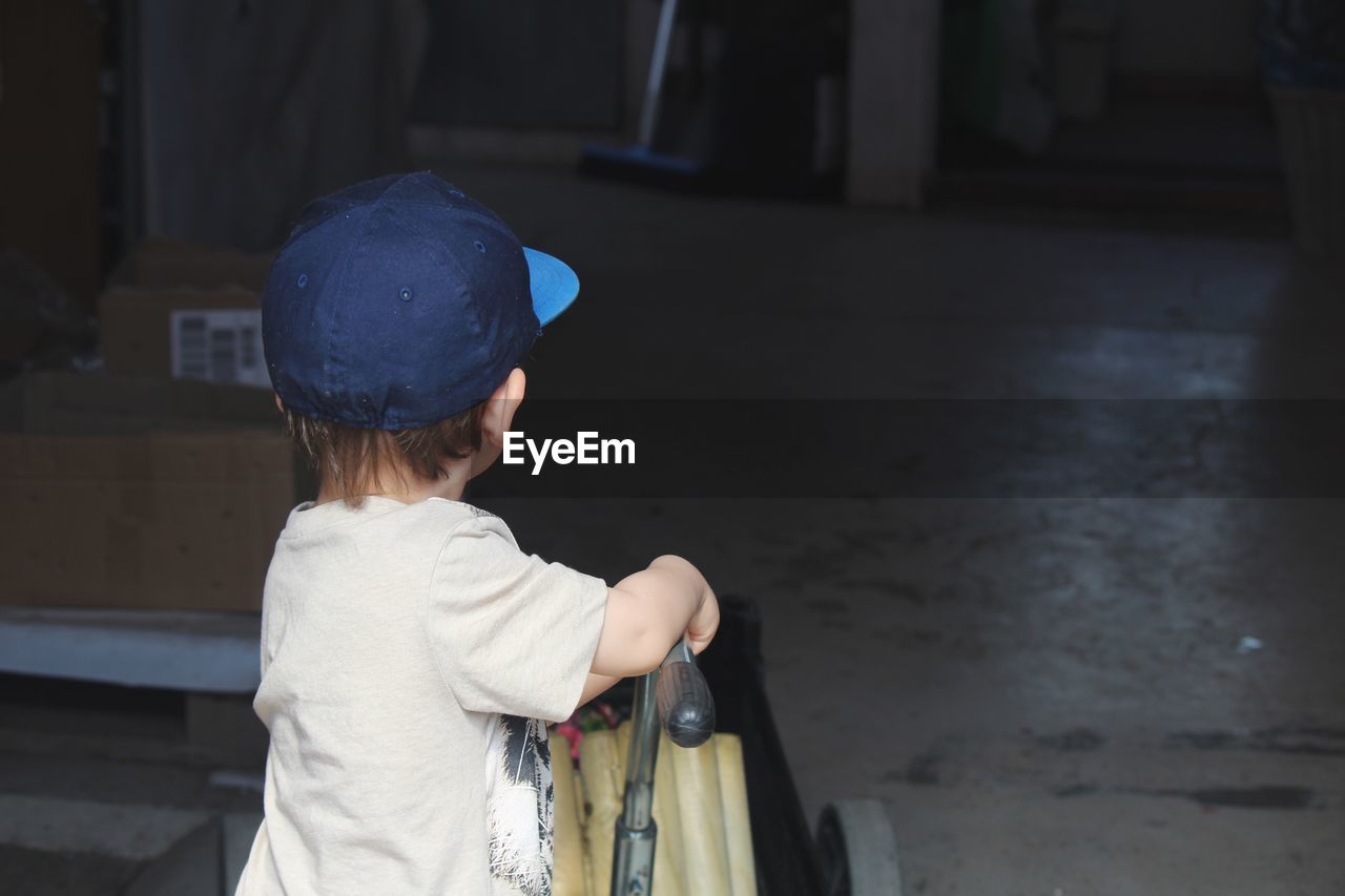 Side view of boy wearing cap pushing cart at home