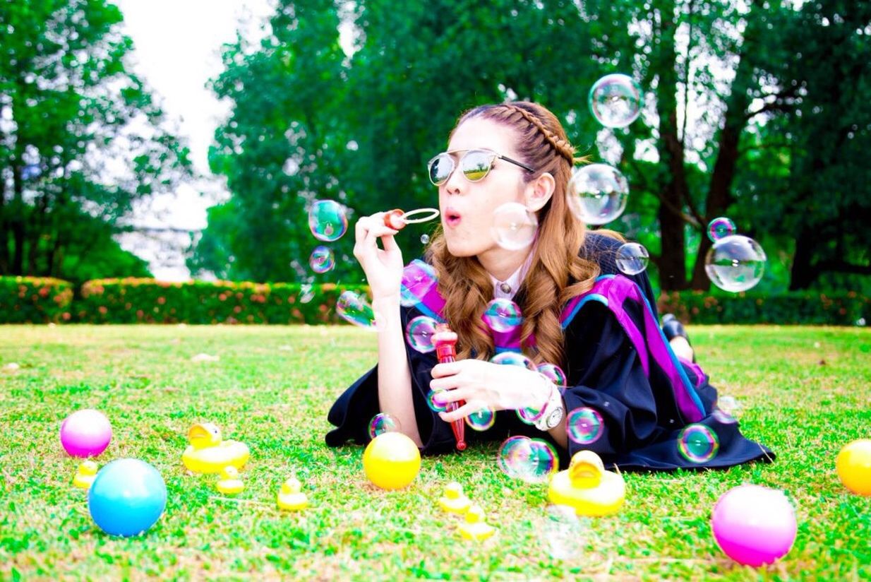 Young woman in graduation gown while blowing soap bubbles