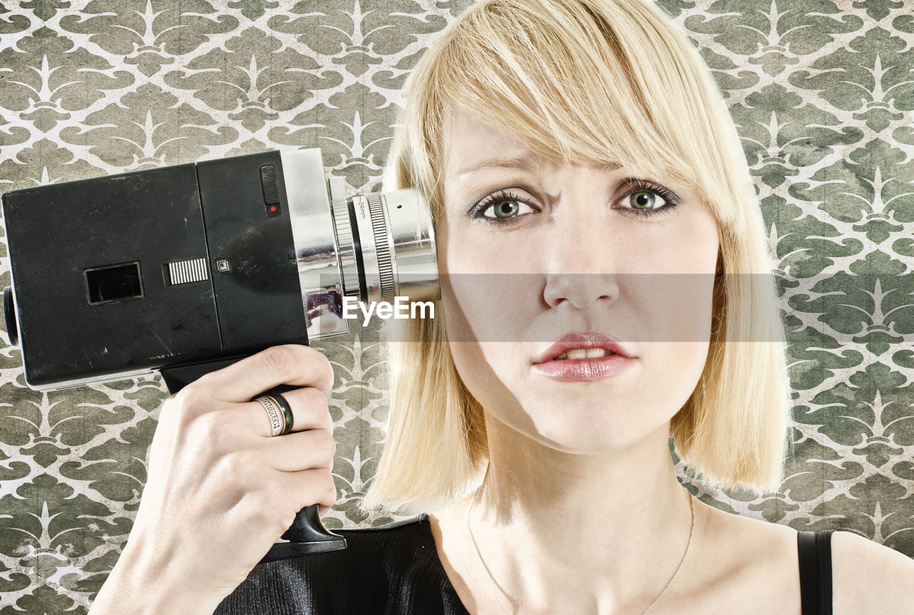 Portrait of woman holding video camera against wall