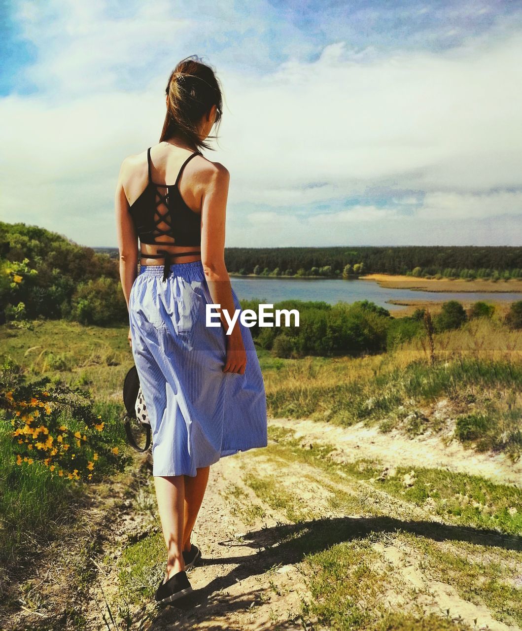 Rear view of woman walking on field against sky