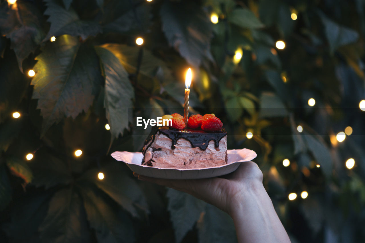 A cake on paper plate with burning candle