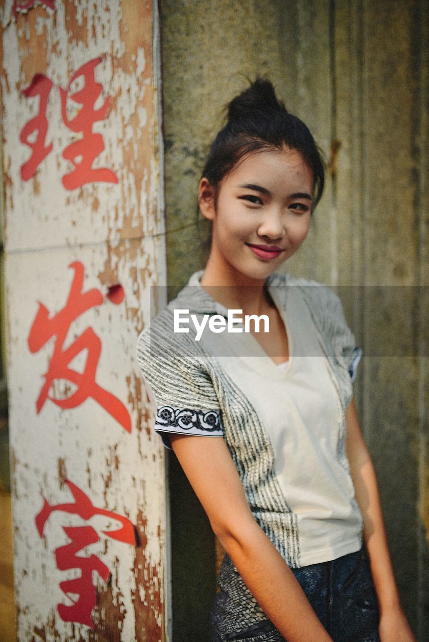 PORTRAIT OF YOUNG WOMAN STANDING AGAINST GRAFFITI