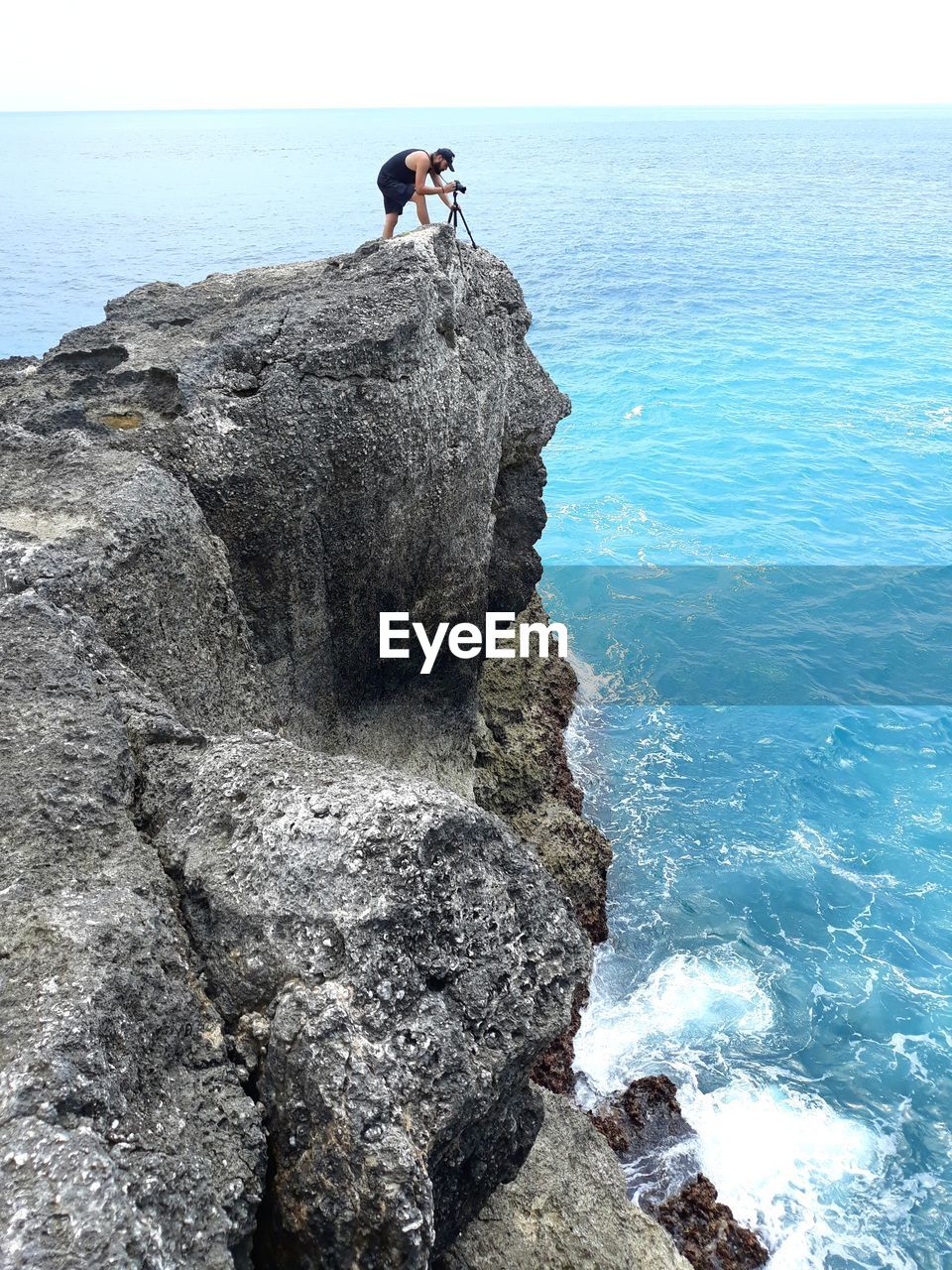 Man standing with camera on cliff by sea