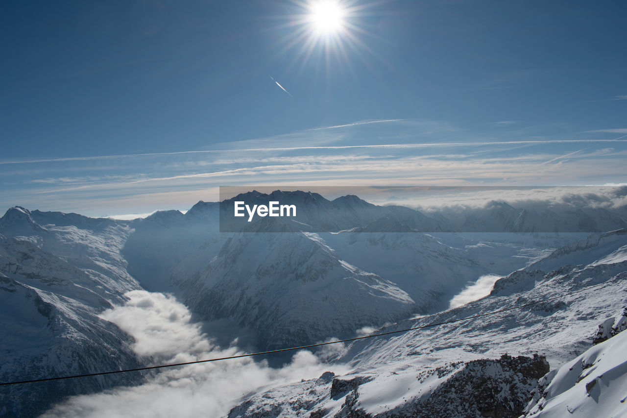 snow, mountain, scenics - nature, cold temperature, winter, environment, sky, beauty in nature, mountain range, landscape, nature, sun, sunlight, snowcapped mountain, travel, tranquility, tranquil scene, travel destinations, cloud, no people, sunbeam, lens flare, non-urban scene, outdoors, blue, land, winter sports, day, mountain peak, tourism, idyllic