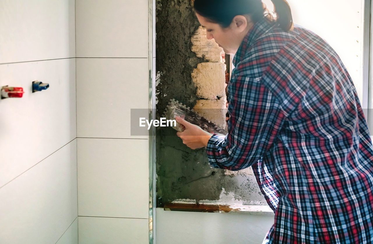 Female mason leveling cement with a trowel to tile the wall