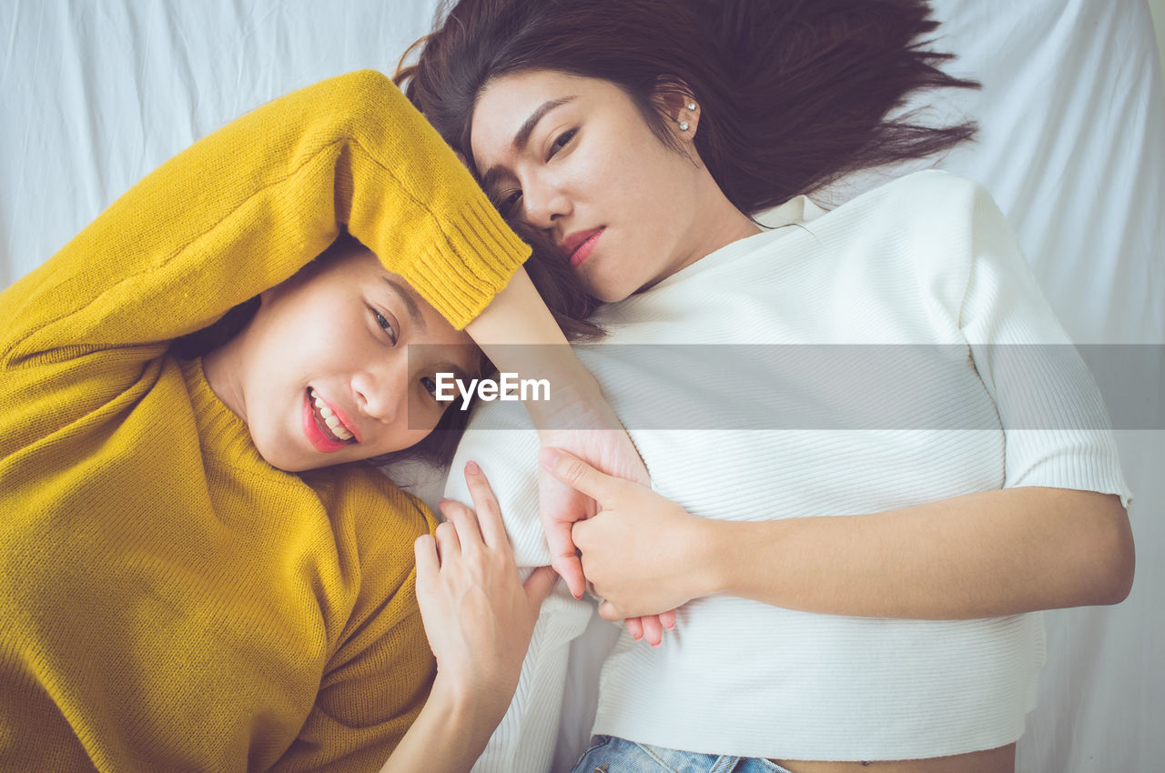 High angle portrait of sisters lying on bed at home