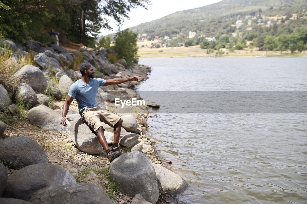 Full length of man sitting by river on rock