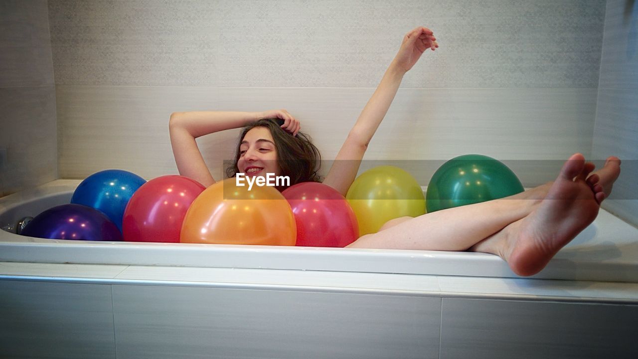 Happy woman in bath tub with balloons in bathroom