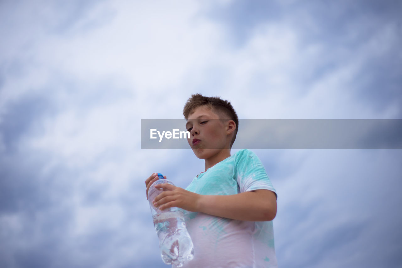 Boy with a bottle of clean water on the background of the sky. thirst. drink water.
