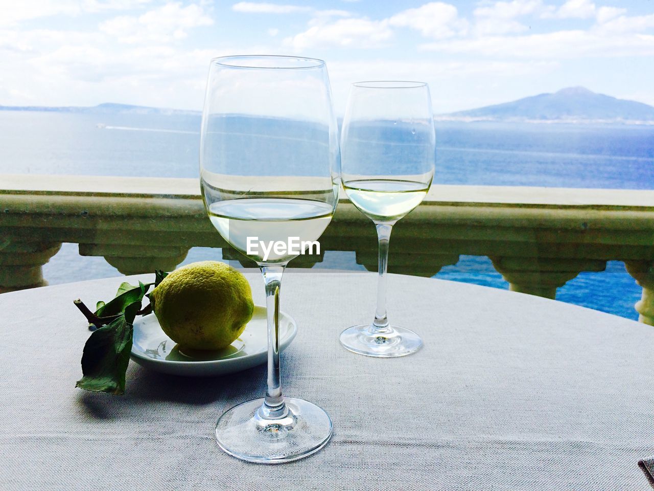 Wineglasses and fruit on table against sea