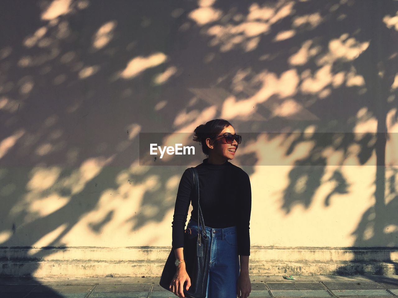 Smiling woman wearing sunglasses while standing against wall