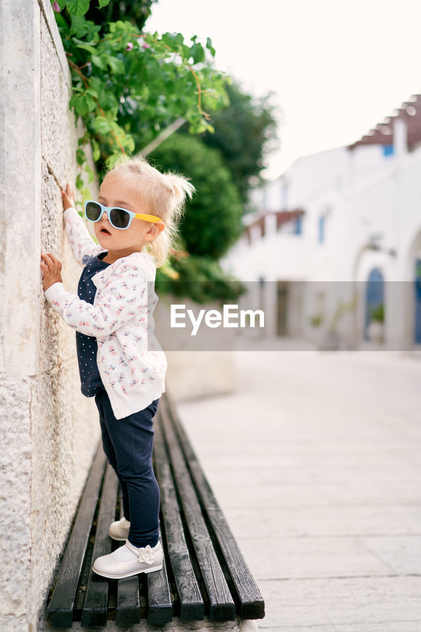 portrait of young woman wearing sunglasses while standing on footpath