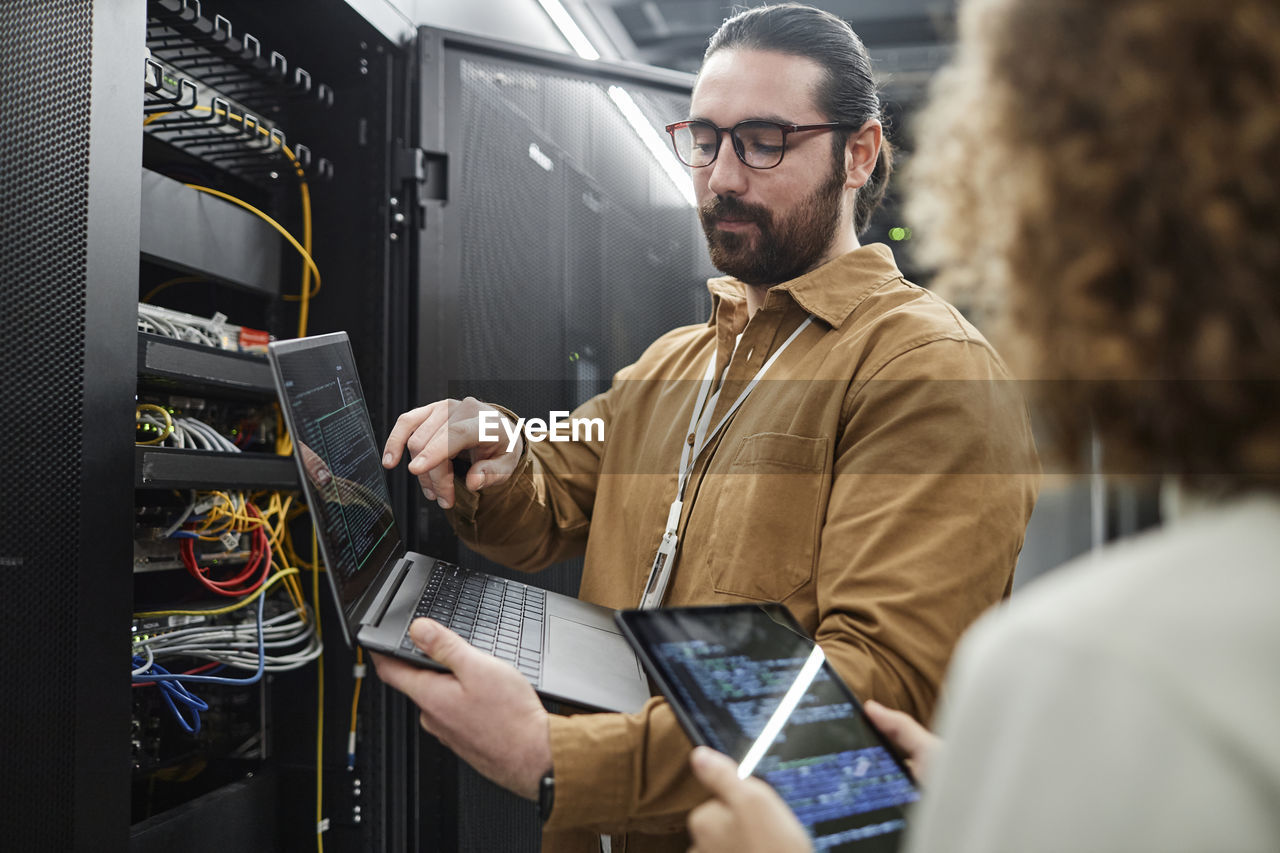 It professionals discussing over data on laptop and tablet pc in server room