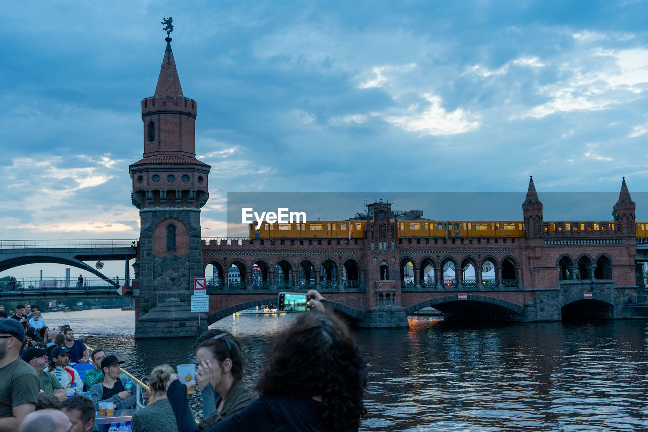 GROUP OF PEOPLE IN FRONT OF BRIDGE OVER RIVER