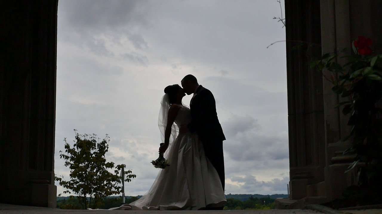 Bride and groom kissing against cloudy sky
