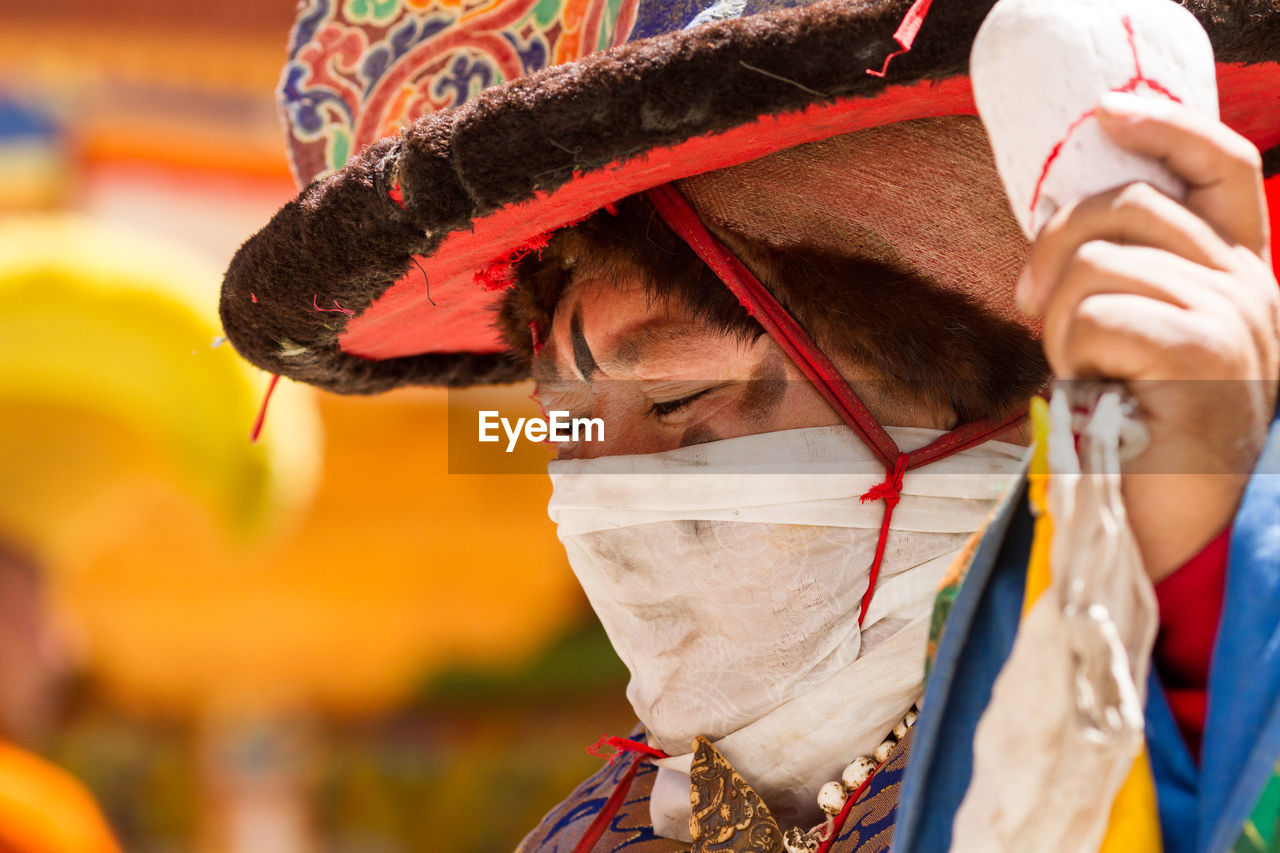 CLOSE-UP PORTRAIT OF MAN WEARING HAT HOLDING MASK