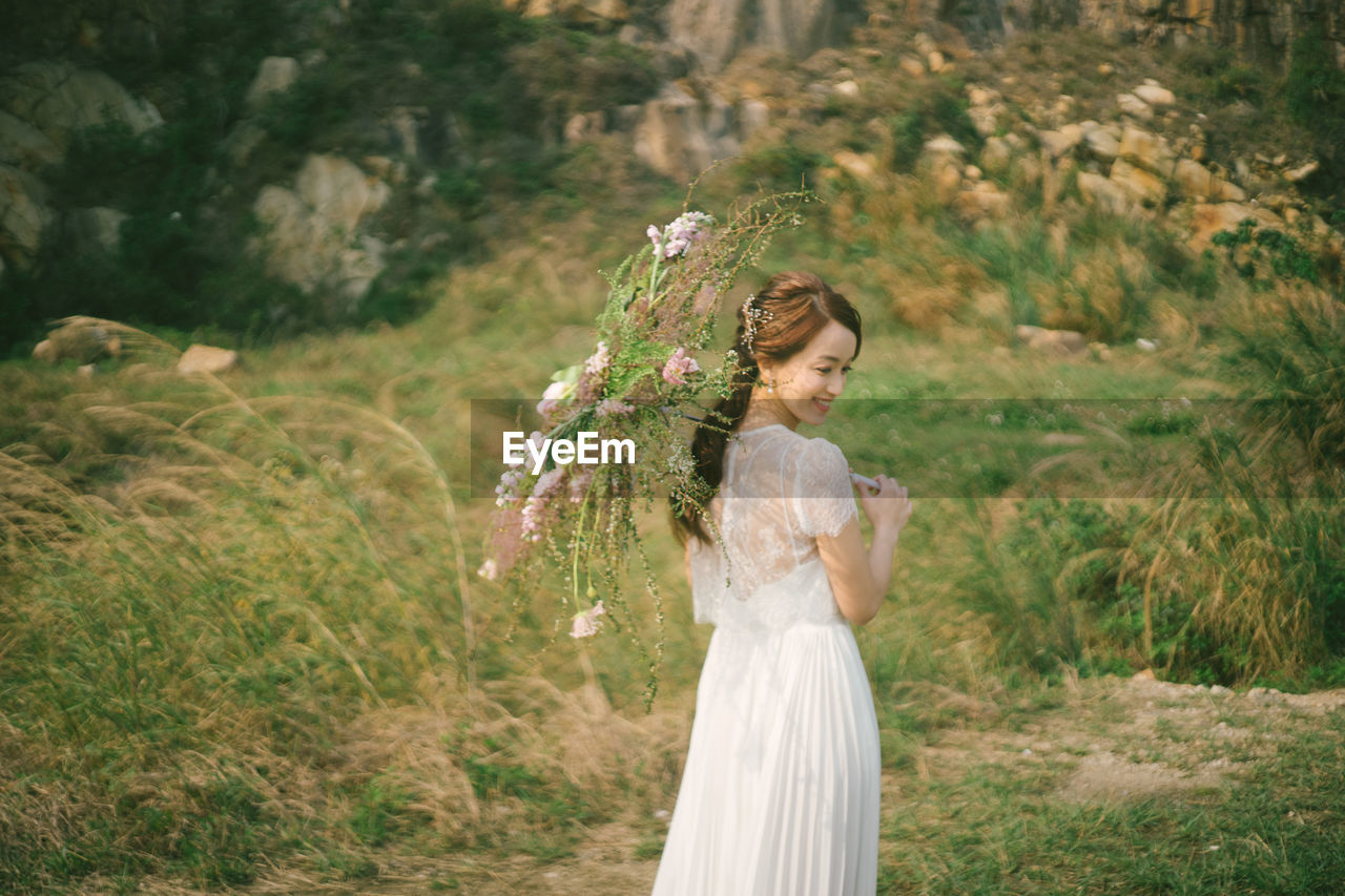 Side view of bride holding umbrella while standing on grassy field