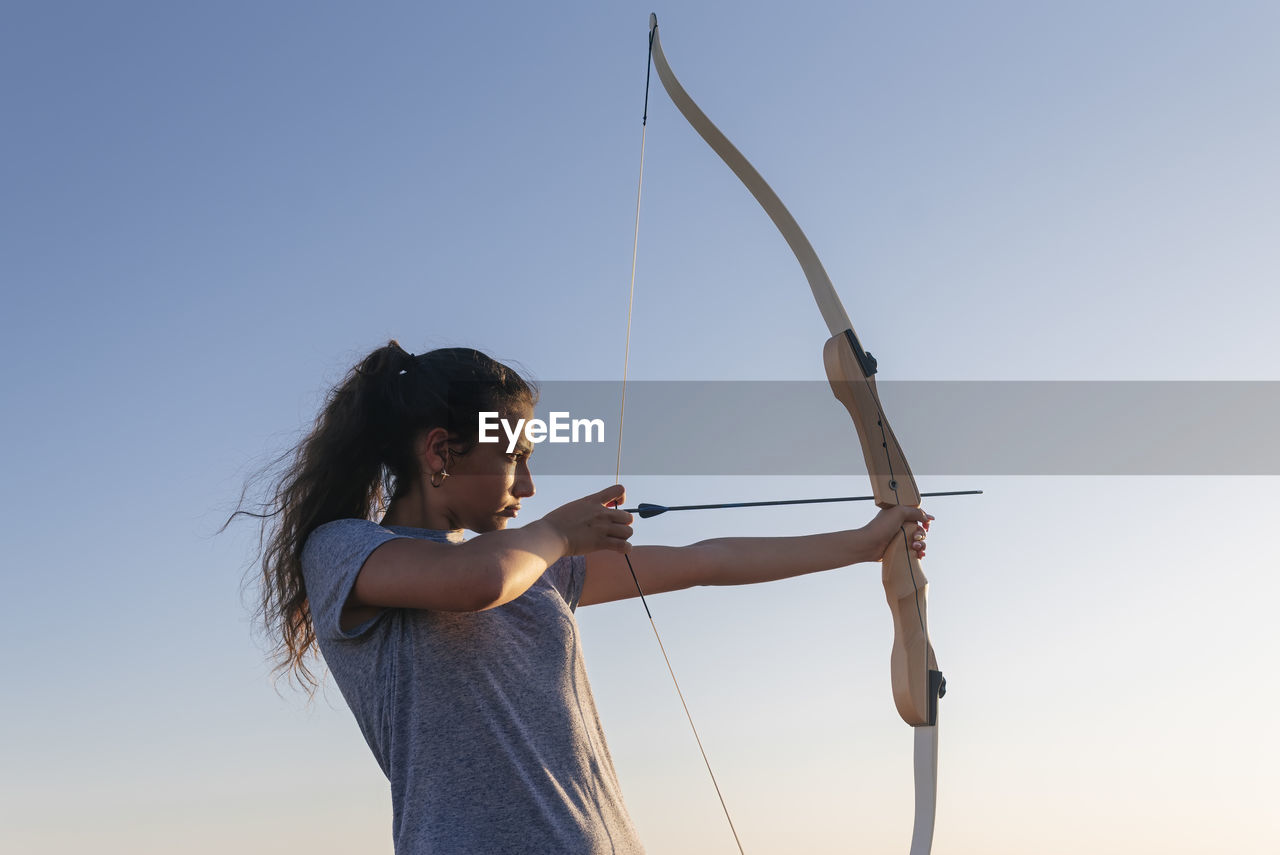 Woman practicing archery by clear sky