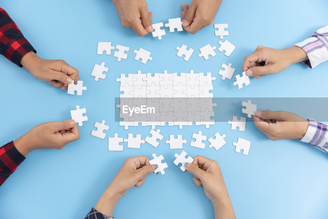 group of people, cooperation, teamwork, hand, men, togetherness, jigsaw piece, puzzle, adult, shape, strategy, jigsaw puzzle, business, finger, unity, communication, solution, partnership - teamwork, young adult, women, group, planning, coworker, businessman, blue, organization, geometric shape, friendship, indoors, business strategy, high angle view, medium group of people, community, circle, blue background