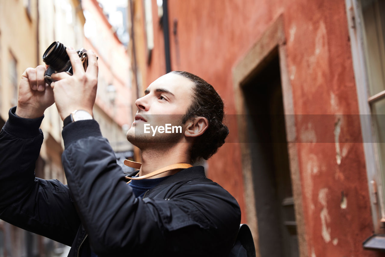 Close-up of young man with camera standing against buildings