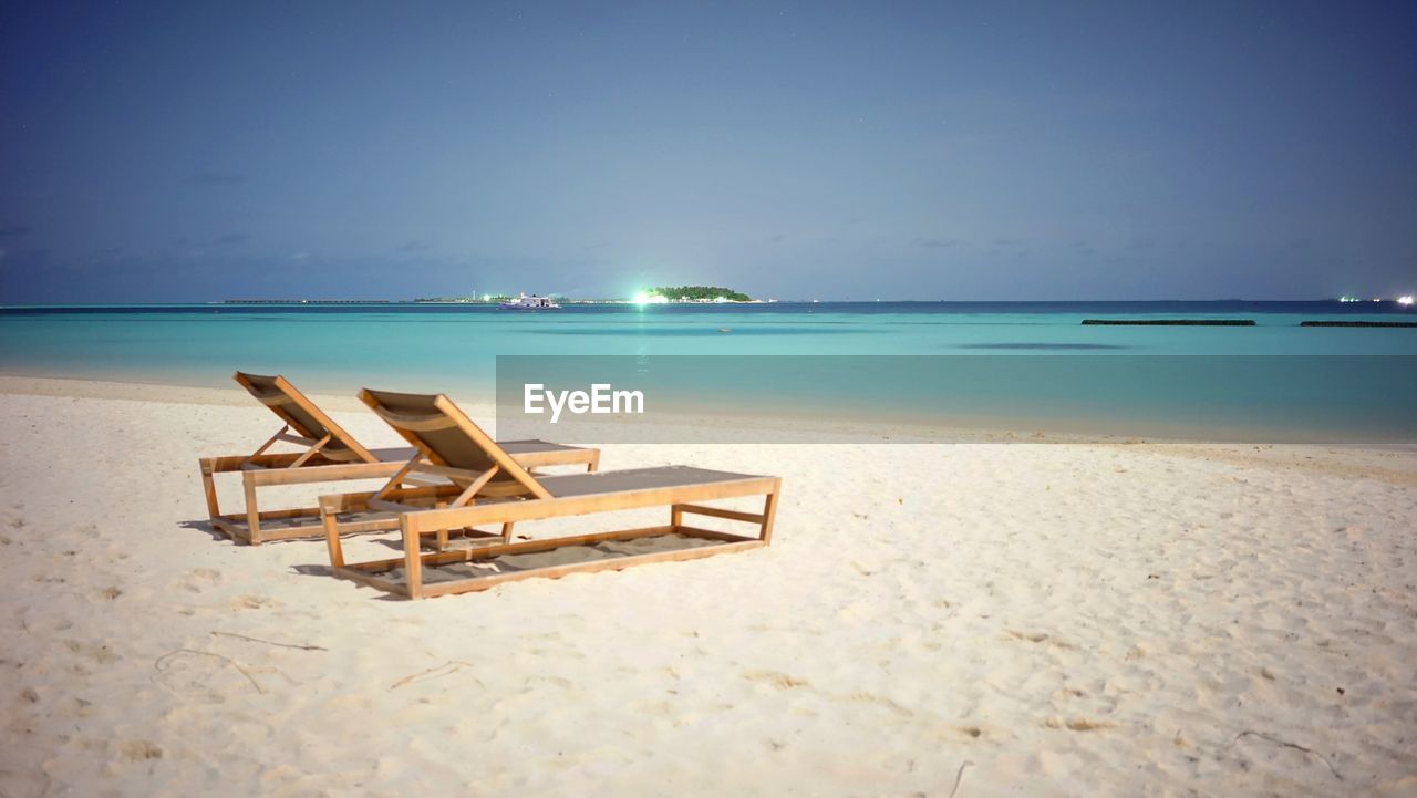 DECK CHAIRS ON BEACH AGAINST SKY
