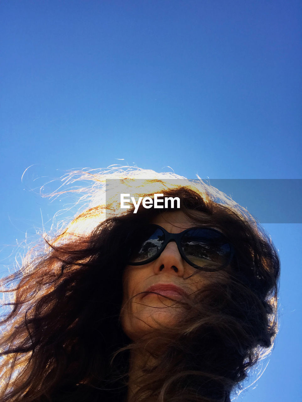 blue, portrait, sky, one person, long hair, adult, glasses, clear sky, hairstyle, headshot, women, low angle view, fashion, nature, sunglasses, young adult, human hair, copy space, human face, wind, brown hair, sunlight, sunny, front view, leisure activity, day, lifestyles, human head, tousled hair, outdoors, female, looking at camera, looking, smiling, close-up, looking up, happiness