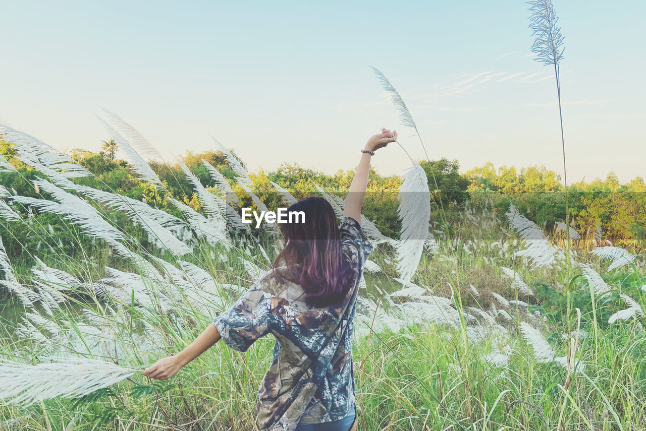 Woman standing by plants on field against sky