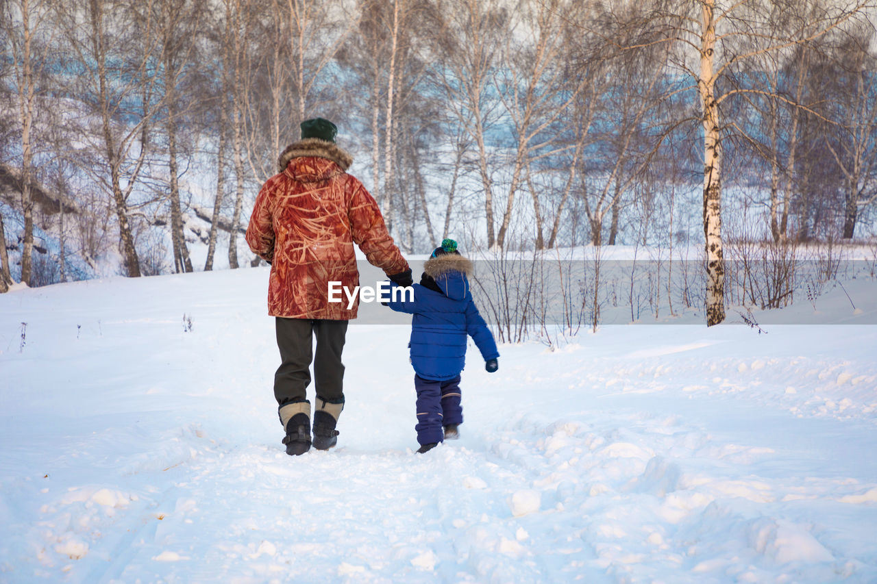 Rear view of father and son walking on snow covered landscape