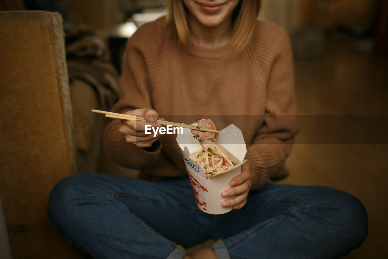 Midsection of woman eating food while sitting on floor at home