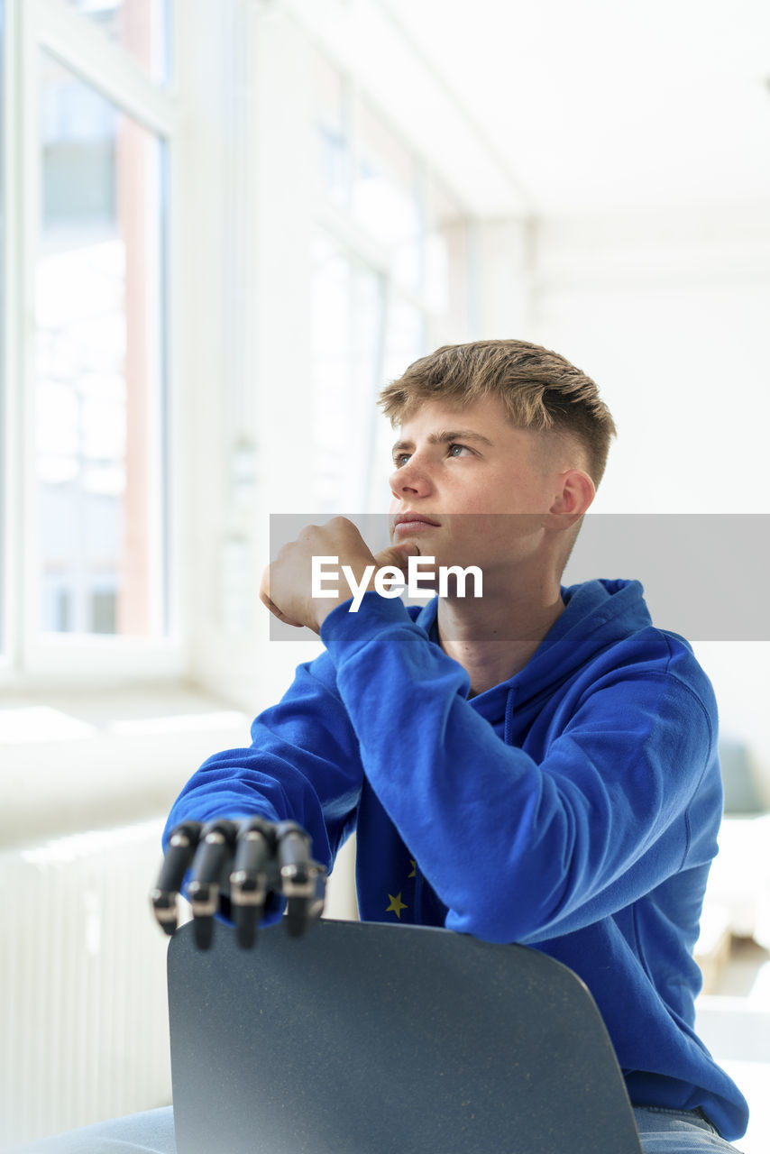 Thoughtful teenage boy with amputated arm sitting on chair