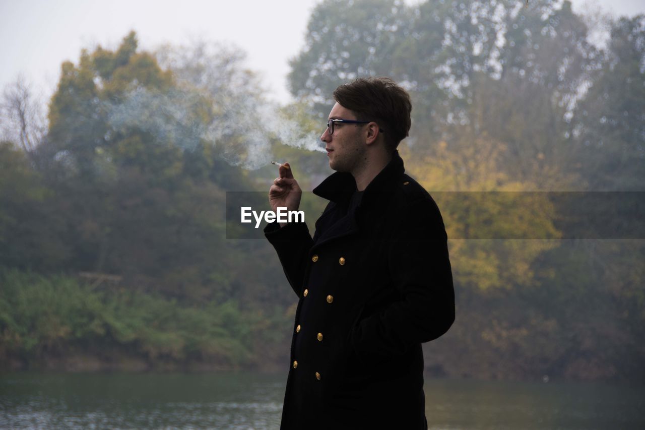 Young man smoking by lake