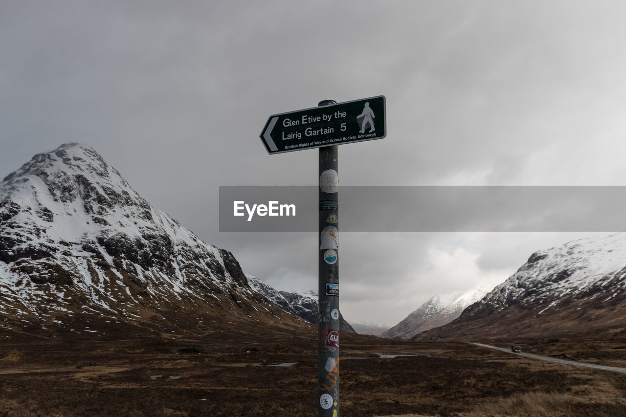 ROAD SIGN BY SNOWCAPPED MOUNTAINS AGAINST SKY