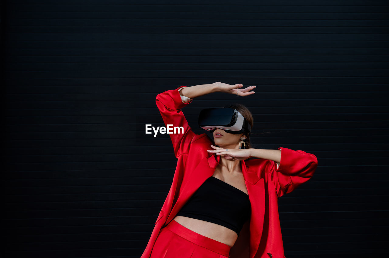 Elegant woman in a red suit using virtual reality goggles on a black background